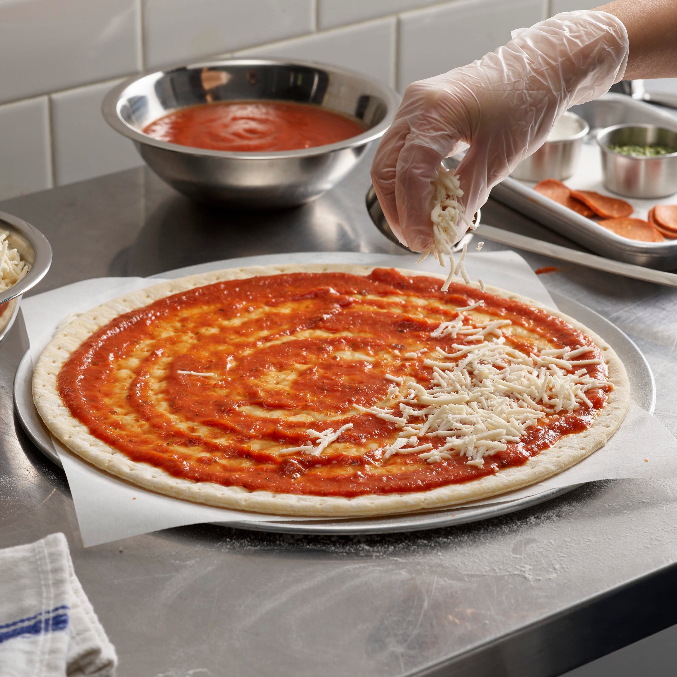 Person preparing a pizza with tomato sauce and cheese on a kitchen counter.